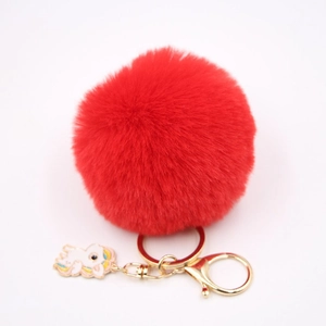 Détail du porte-clés pompon rouge avec breloque licorne dorée et anneau en métal doré