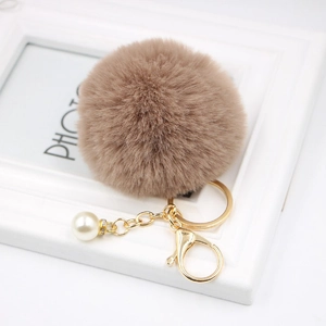 Detailed macro view of khaki faux fur pompom keychain with pearl charm and golden clasp