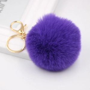 Detail view of a fluffy purple faux rabbit fur pompom keychain with gold metal clasp