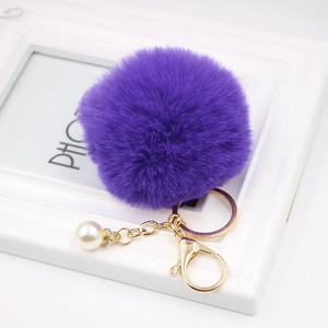 Detailed view of purple faux fur pompom keychain with golden clasp and pearl charm