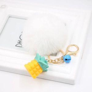 Detail of white faux fur pompom keychain with yellow pineapple charm and golden clasp