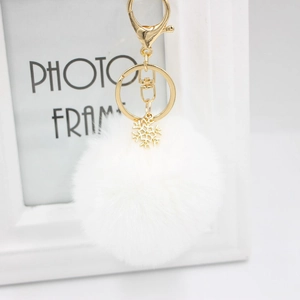 Detailed macro view of white plush pompom keychain with golden metal snowflake charm