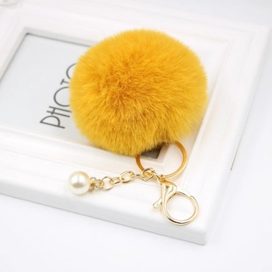Detail view of yellow faux fur pompom keychain with gold lobster clasp and pearl accent
