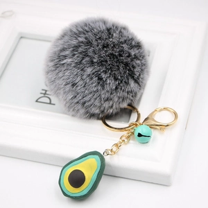 Detail of avocado plush keychain with grey pompom, gold metal clip, and small blue bell
