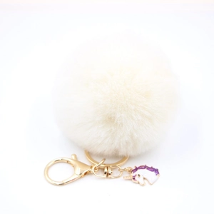 Detail of fluffy white pompom keychain with golden clasp and unicorn enamel charm