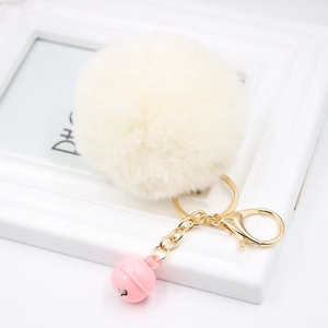 Macro detail of fluffy cream faux fur keychain with golden clasp and pink bell