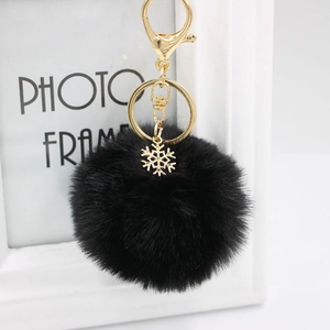 Detail of black fluffy faux fur pompom keychain with golden snowflake alloy charm