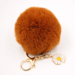 Détail d'un porte-clés pompon en fausse fourrure caramel avec breloque marguerite et doré