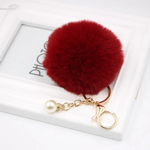 Detail of burgundy faux fur pompom keychain with gold lobster clasp and pearl charm