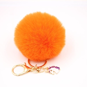 Detailed view of orange faux fur pompom keychain with golden unicorn enamel charm