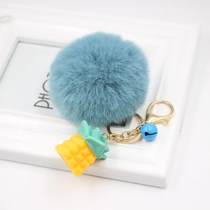 Close-up of fluffy grey-blue pompom keychain with golden pineapple charm and small blue bell
