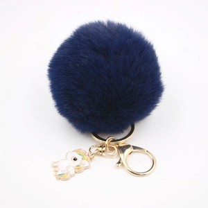 Détail d'un pompon en fausse fourrure bleu foncé avec pendentif licorne émaillé et fermoir