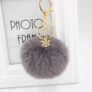 Detailed view of gray plush pompom keychain with golden snowflake charm and lobster clasp