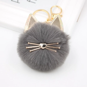 Detailed close-up of a plush grey cat pompom keychain with golden ears and glitter accents