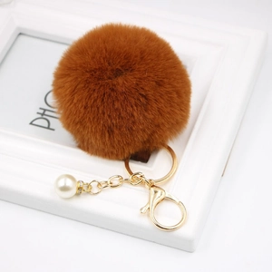 Close-up of brown faux fur pompom keychain with golden metal clasp and white pearl charm