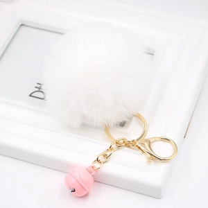Detail of white faux fur keychain with a pink bell and gold clasp on white background