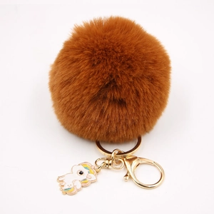 Détail d'un pompon en fausse fourrure marron avec fermoir doré et breloque licorne