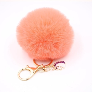 Macro detail of an orange faux fur pompom keychain with a white unicorn charm and gold clasp