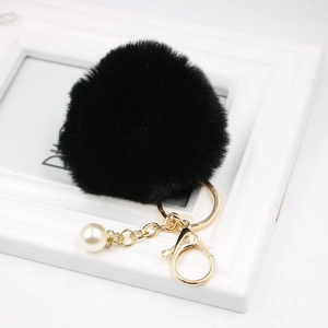 Detail of black faux fur pompom keychain with gold hardware and white pearl charm