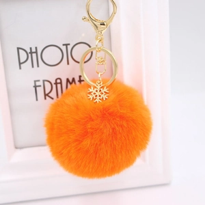Detail of a bright orange fluffy pom pom keychain with a gold snowflake charm and clasp
