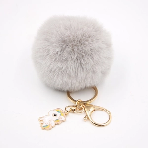 Détail d'un porte-clés pompon en fausse fourrure grise avec breloque licorne en émail doré