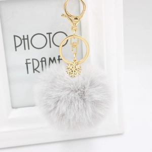 Detail of light grey faux fur pom pom keychain with a gold snowflake charm and lobster clasp
