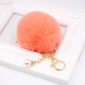 Close-up of pink fluffy pompom keychain with gold lobster clasp and white pearl detail