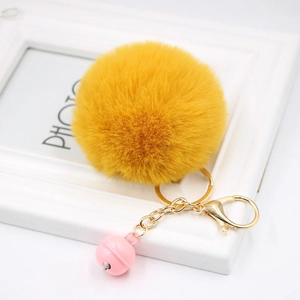 Close-up of fluffy yellow faux fur pompom keychain with golden ring and pink bell