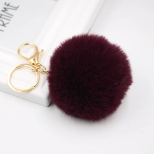 Close-up of fluffy burgundy faux rabbit fur pom pom with a golden metal keychain clasp