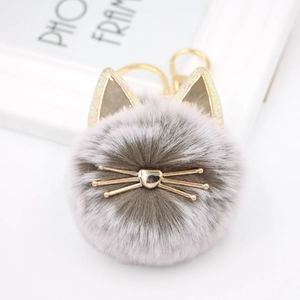 Close-up of cute grey plush cat pompom keychain with golden metal whiskers and heart nose