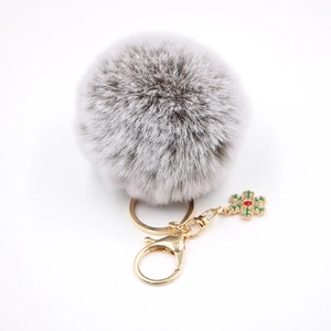 Détail d'un pompon en fausse fourrure grise avec breloque flocon dorée et cristal rouge