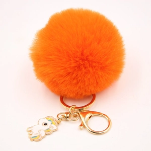 Détail macro du pompon en fausse fourrure orange vif avec charm de licorne dorée