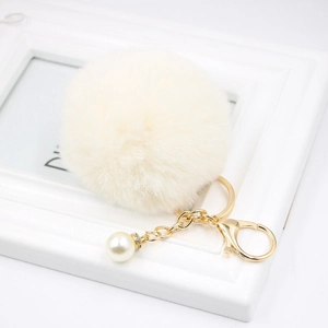 Close-up of a white fluffy pompom keychain with gold hardware and a pearl charm