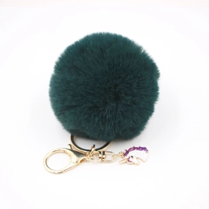 Detail of dark green pompom keychain with gold hardware and enamel unicorn charm