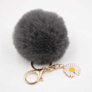 Vue détaillée du porte-clés pompon gris avec fermoir doré et charm marguerite blanche