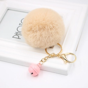 Detailed macro view of soft cream faux fur pompom keychain with golden clasp and pink bell