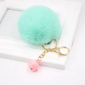 Close-up of mint green faux fur pompom keychain with gold carabiner and pink bell charm