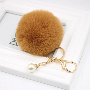 Detail of a brown faux fur pompom keychain with golden metal clasp and pearl charm