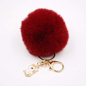 Détail d'un pompon en peluche bordeaux avec fermoir doré et breloque licorne élégante