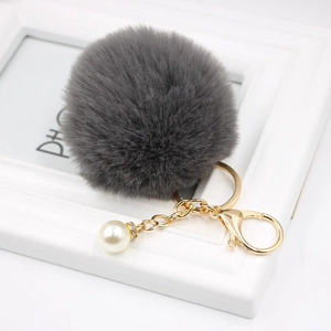 Close-up of grey faux fur pompom keychain with white pearl charm and golden clasp detail