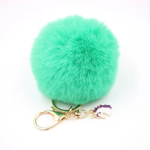 Detail of mint green faux fur pompom keychain with golden clip and unicorn charm