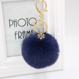 Close-up of a dark blue plush faux fur ball keychain with a gold snowflake pendant and clasp