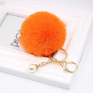 Detail of an orange faux fur keychain with a gold chain and white pearl accent