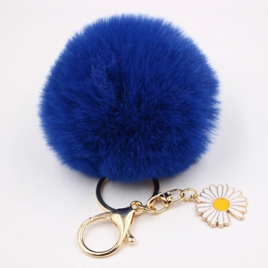 Détail d'un porte-clés pompon bleu roi avec fermoir doré et pendentif fleur de marguerite
