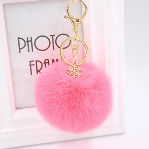 Close-up of pink fluffy pompom keychain with golden metal snowflake pendant and lobster clasp