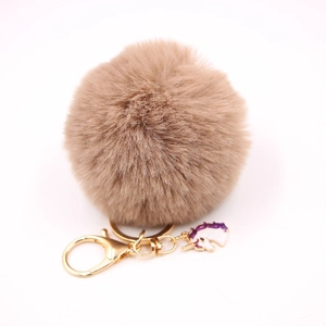 Detail of tan faux fur pompom keychain with gold lobster clasp and unicorn charm