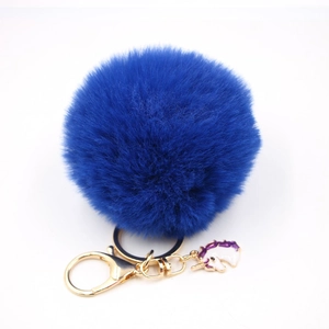 Close-up of fluffy dark blue pompom keychain with golden lobster clasp and unicorn charm