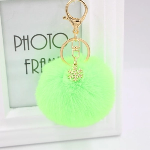 Detail view of neon green plush pompom keychain with golden snowflake charm and ring