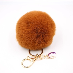 Detail of caramel faux fur pompom keychain with golden clip and purple unicorn charm