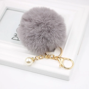 Macro detail of a soft grey faux fur pompom keychain with gold chain and pearl accent